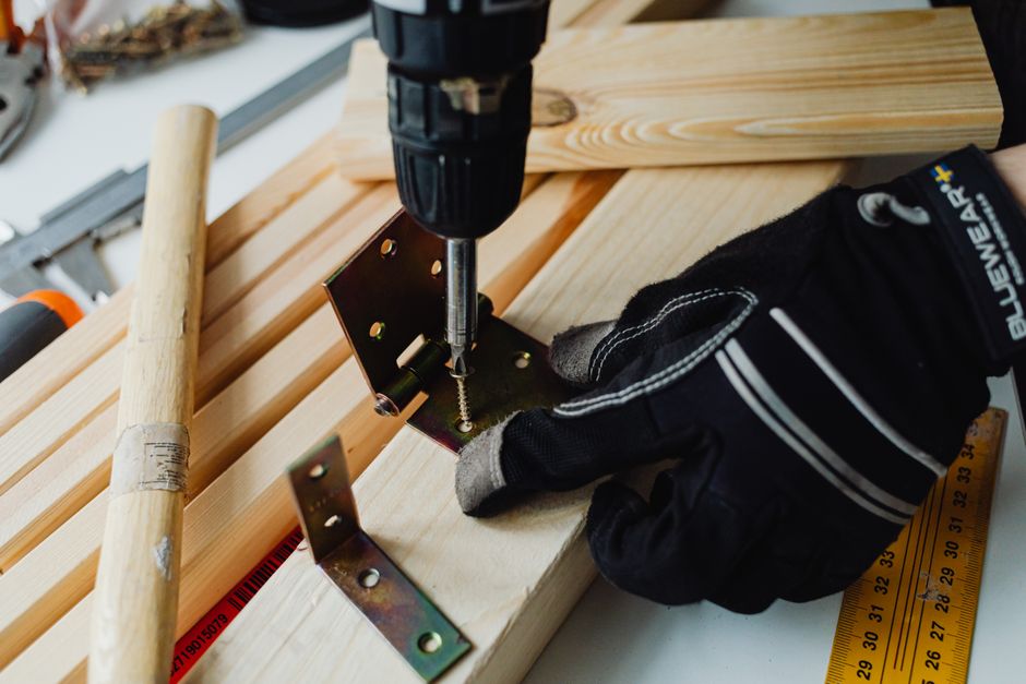 Power drill with bracket and safety gloves on woodworking project for garage door reinforcement