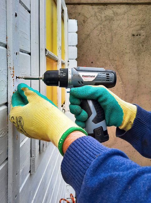 Construction worker using a power drill on a wall showing garage door strut installation technique