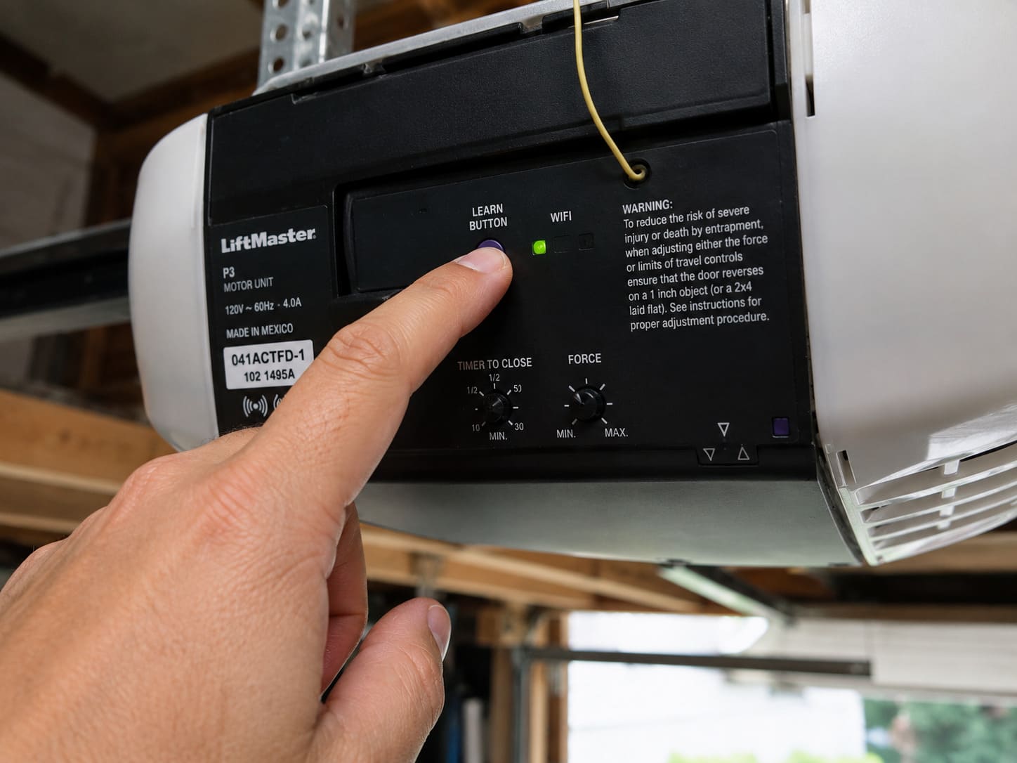 Hand pressing the Learn button on the back of a LiftMaster garage door opener motor unit