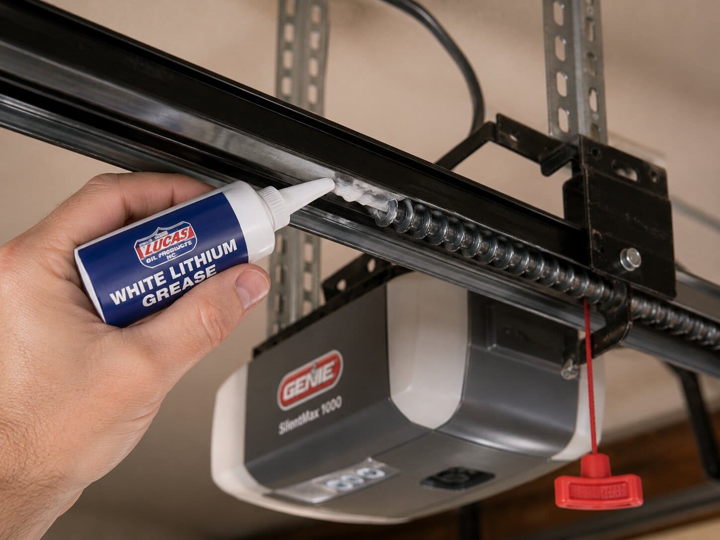 Hand applying white lithium grease to a screw drive garage door opener rail