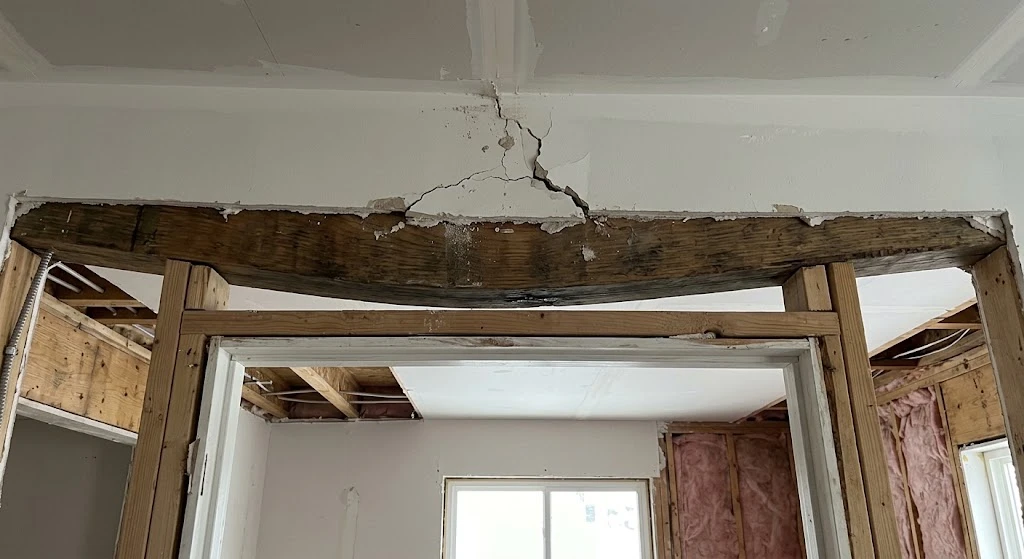 Sagging header beam with cracked drywall above a door opening